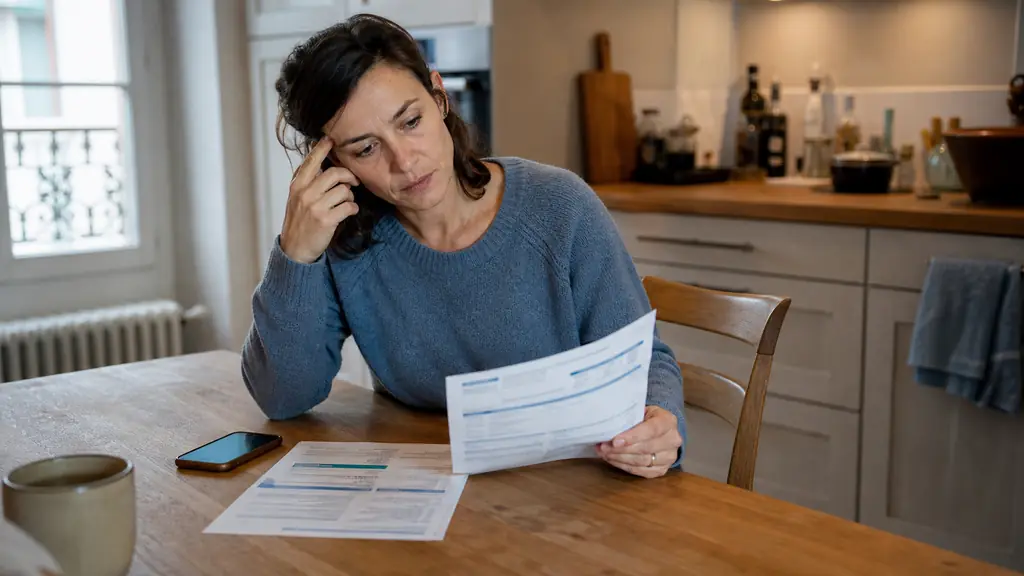 Adult at a kitchen table reviewing a podiatry estimate beside a health insurance statement and a smartphone, natural daylight, documentary editorial photography, no readable text, no logos