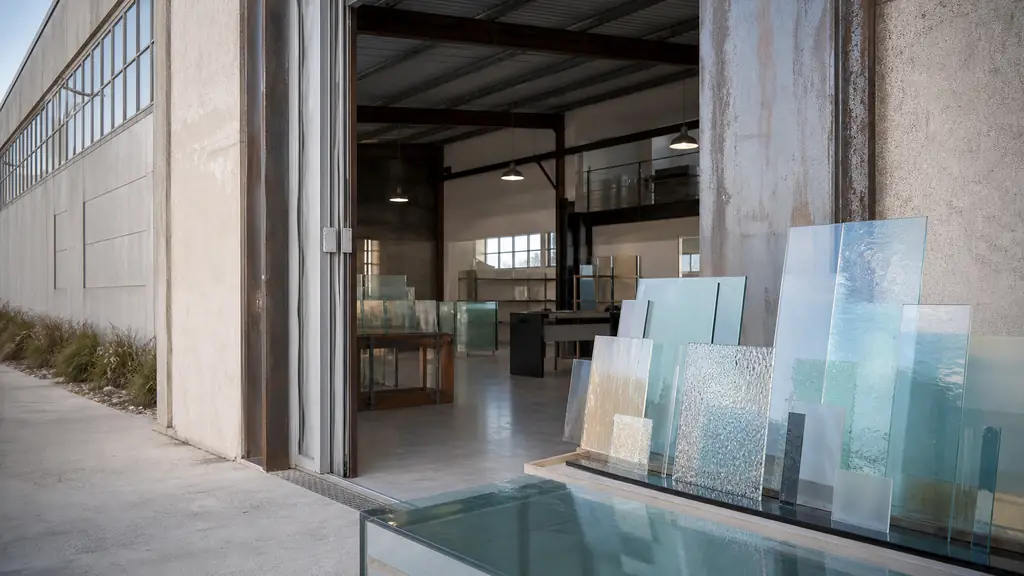 Editorial photograph of the Villemarion industrial area in Riantec, showing a renovated former shipyard workshop entrance and carefully arranged custom glass samples, with no visible text or logos
