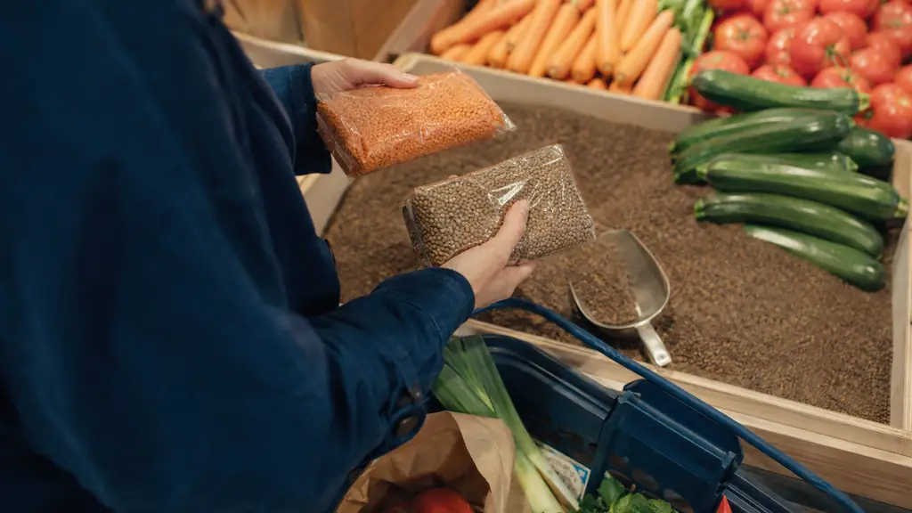 close-up editorial photograph of a shopper comparing two unbranded prepackaged food products beside loose lentils and fresh vegetables in a French grocery store, no visible text or logos