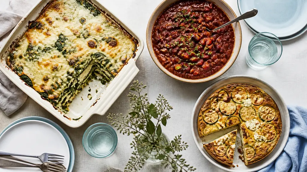 Editorial overhead photograph of a colorful vegetarian table with spinach ricotta lasagna, red bean chili sin carne, and golden courgette feta cake, natural daylight, no text or logo