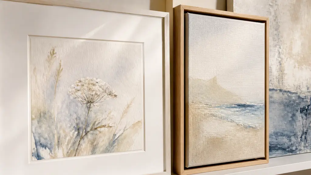 Editorial close-up of a watercolor under anti-reflective glass with an acid-free mat beside a canvas mounted in a slim oak floating frame, visible Dibond print in the background, no text, no logo