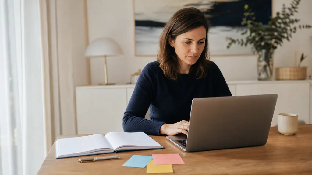 French professional woman reviewing an email on a laptop, with an open conjugation notebook, a pen and three colored study cards on a tidy office desk, editorial photography, no readable text, no logo