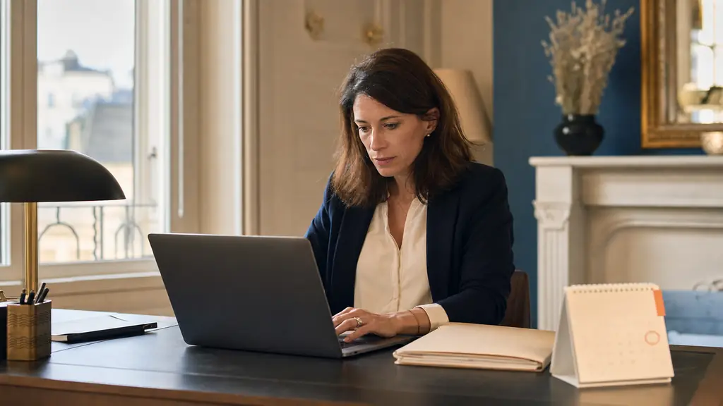 editorial photograph of a professional woman checking an email draft on a laptop beside a client folder and a desk calendar marked for the following day, no visible text or logos