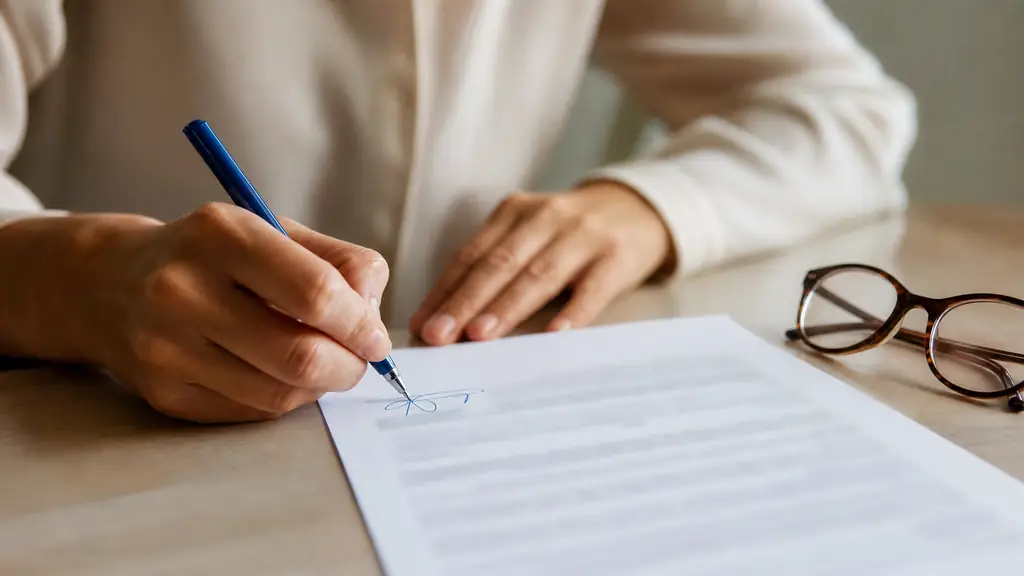 close-up editorial photograph of a woman signing the bottom of a private agreement with a blue pen, reading glasses beside the document, all printed content blurred and unreadable, no text, no logo